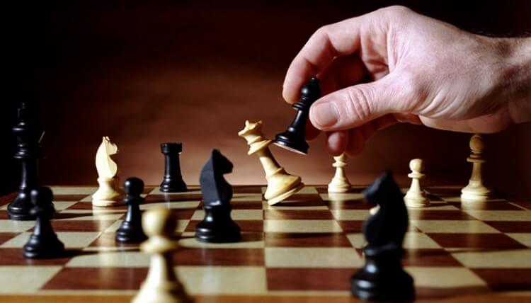 Faça um plano de negócios - tabuleiro de xadrez, mão segurando um peão preto e derrubando a rainha 