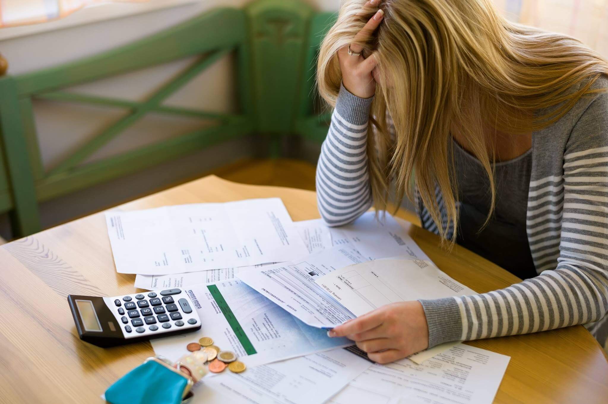 Inadimplência, mulher loira olhando suas contas e com a calculadora na mesa se lamentando