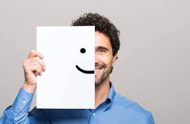 Satisfação pessoal - Homem de cabelo preto, barba rala e camisa azul sorrindo mostrando apenas metade do rosto, a outra metade um papel sorrindo 